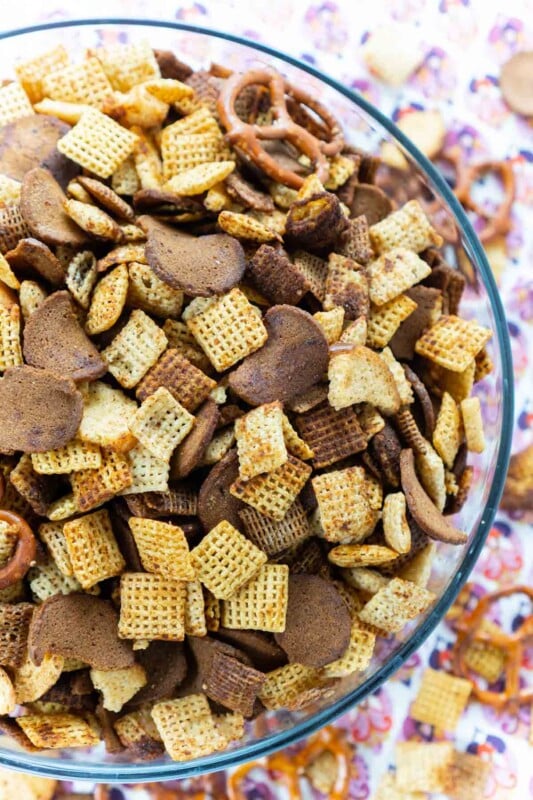Homemade chex mix in a glass bowl with a pink colored napkin behind it