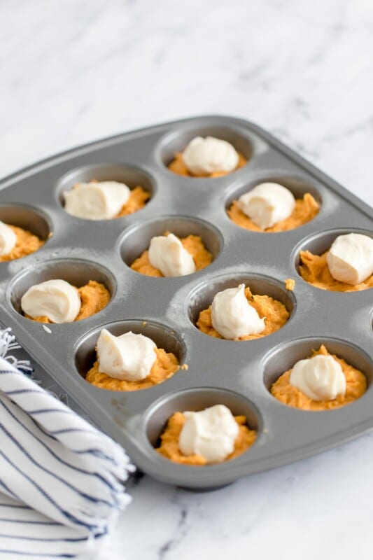 Muffin tins filled with batter for pumpkin cream cheese muffins