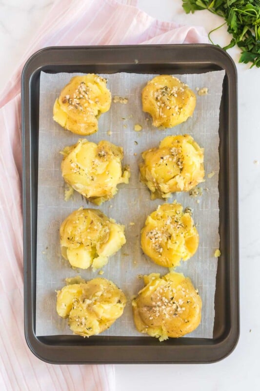 A baking sheet with parchment paper and smashed potatoes