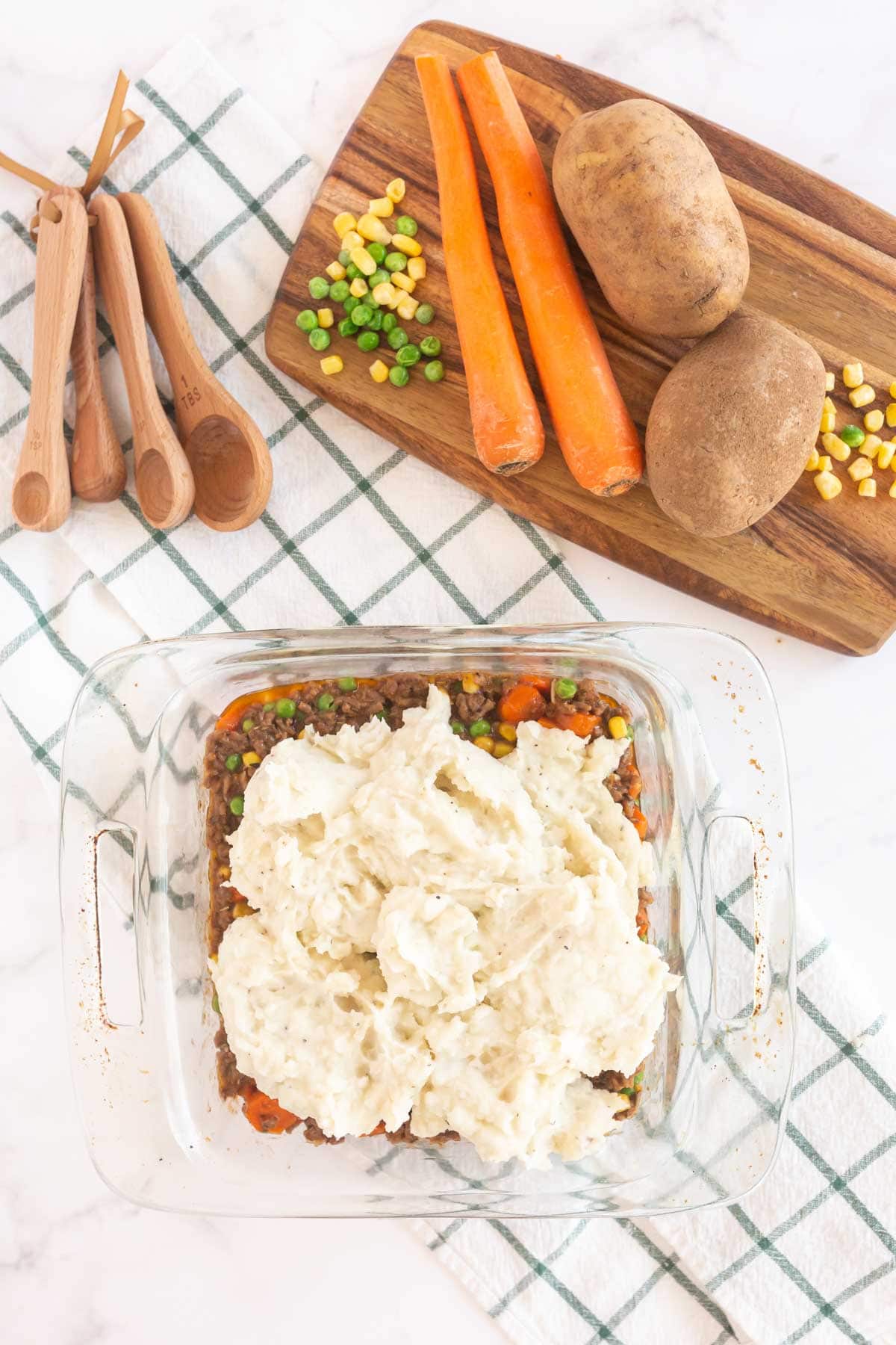 Mashed potatoes on top of shepherd's pie filling in a glass baking dish