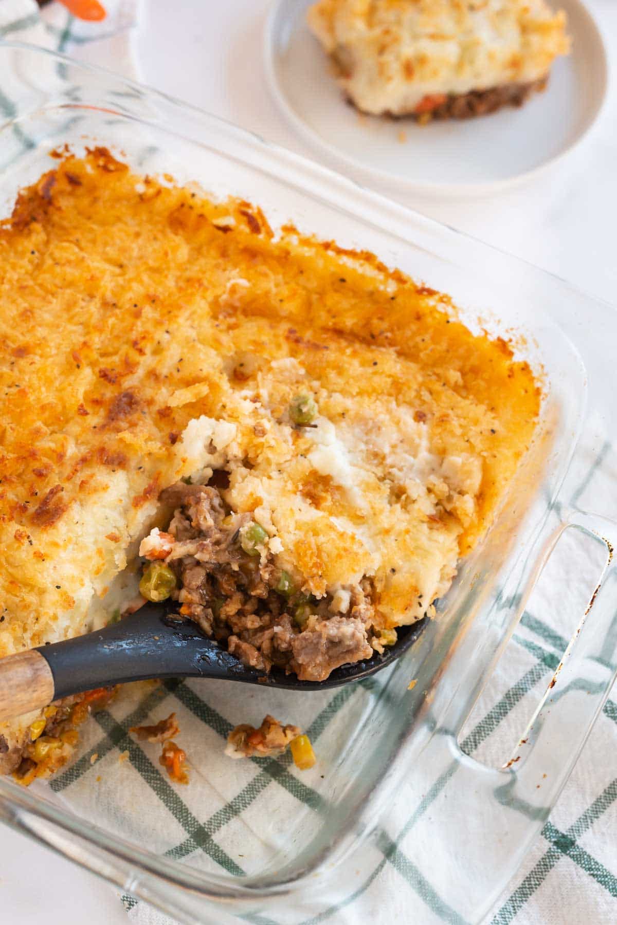 A spoon scooping a scoop of shepherd's pie out of a baking dish