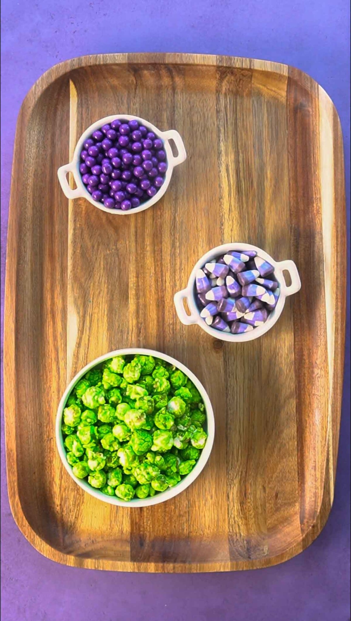 A wood board with three white bowls with candy in them