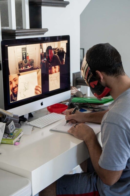 Man drawing a picture in front of a computer with people on zoom