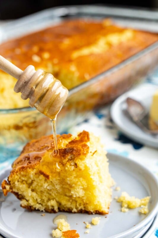 A honey dipper drizzling honey onto a piece of honey cornbread