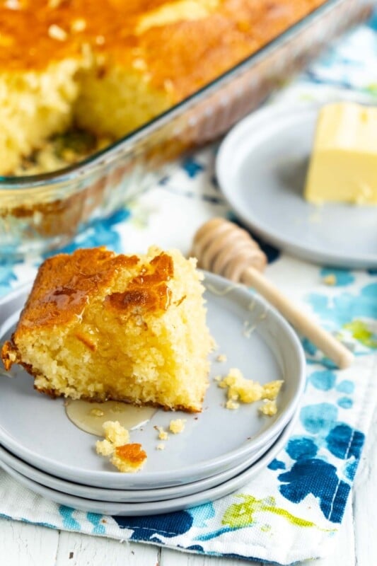 A piece of sweet cornbread on three stacked gray plates with honey and butter