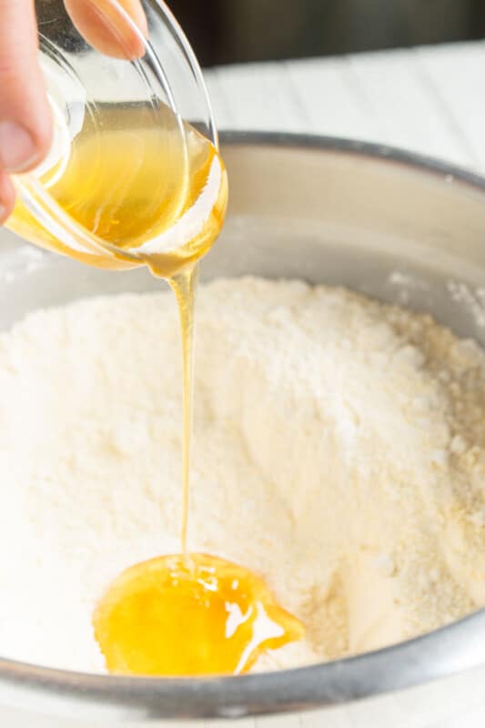 A woman's hand pouring honey into a metal bowl