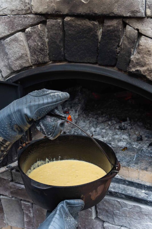 Hands in oven gloves putting a dutch oven of cornbread batter into a brick oven