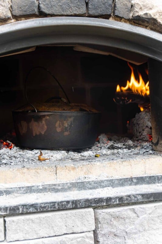 A dutch oven in a brick oven with fire behind