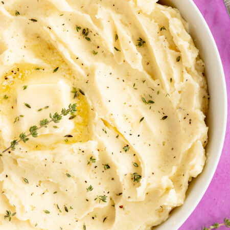 white bowl of mashed potatoes with herbs on top