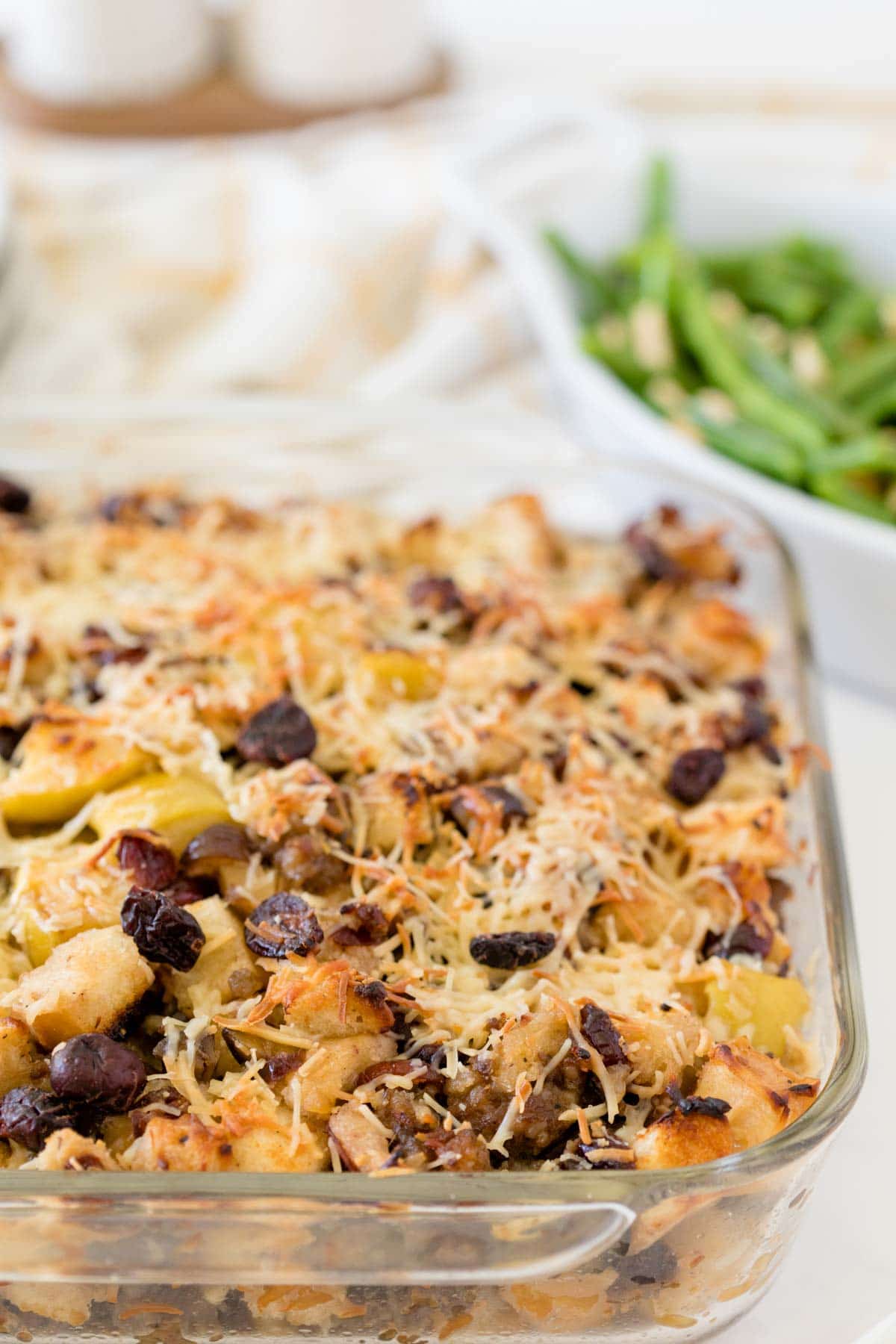 A glass pan of sausage stuffing with green beans in the background