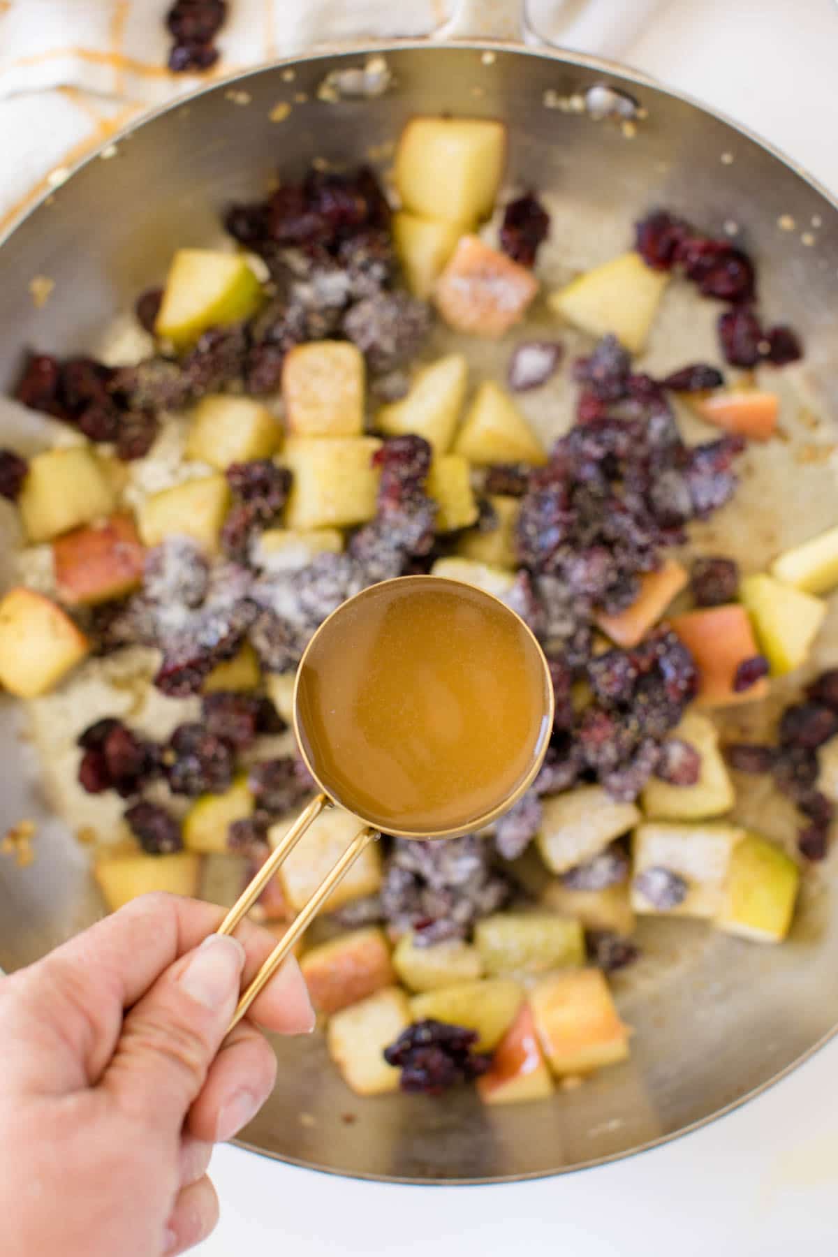 Woman's hand holding chicken broth above a pan of stuffing