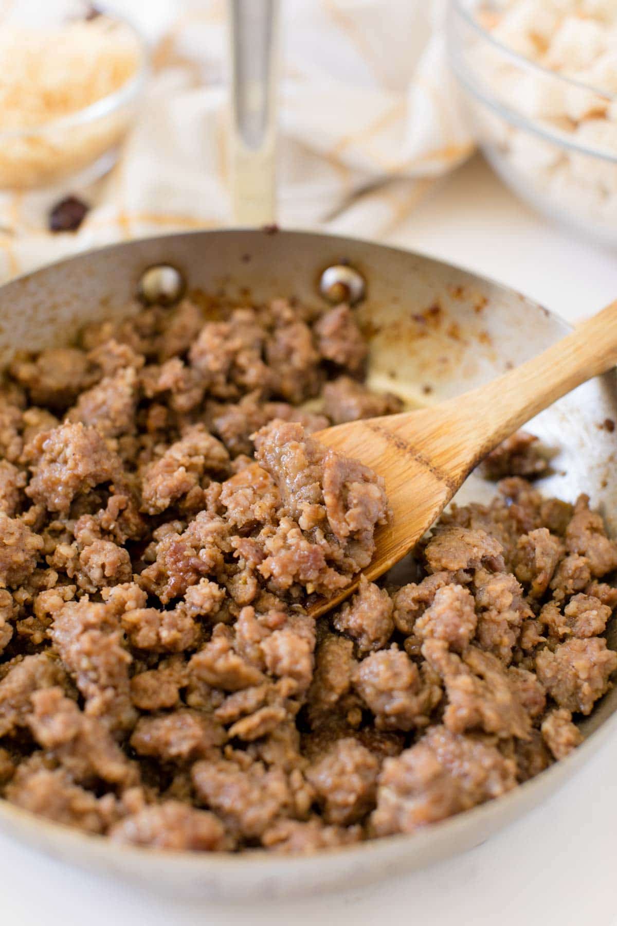 Italian sausage in a metal pan with a wooden spoon