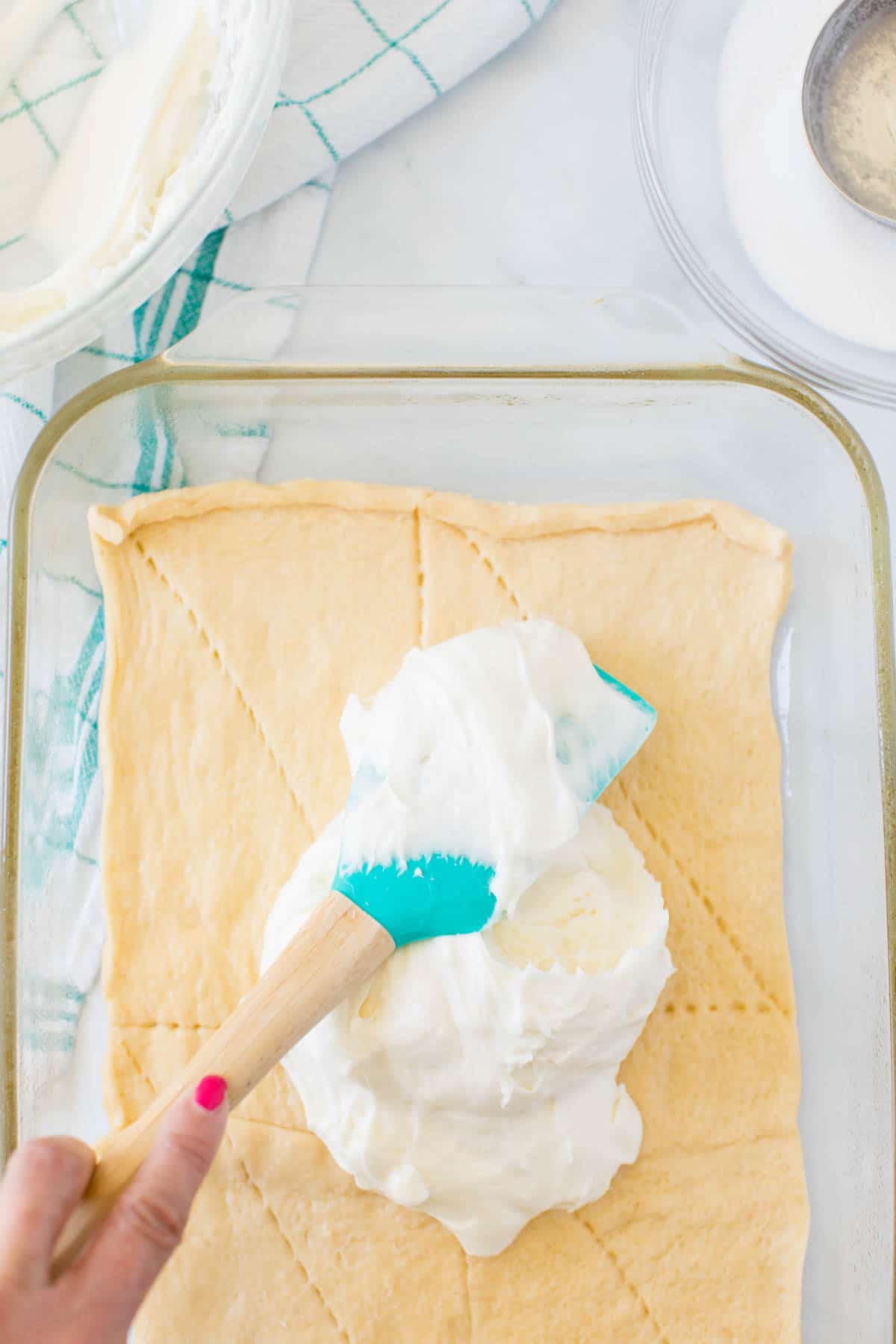 Spatula adding cream cheese mixture to crescent rolls in a baking dish