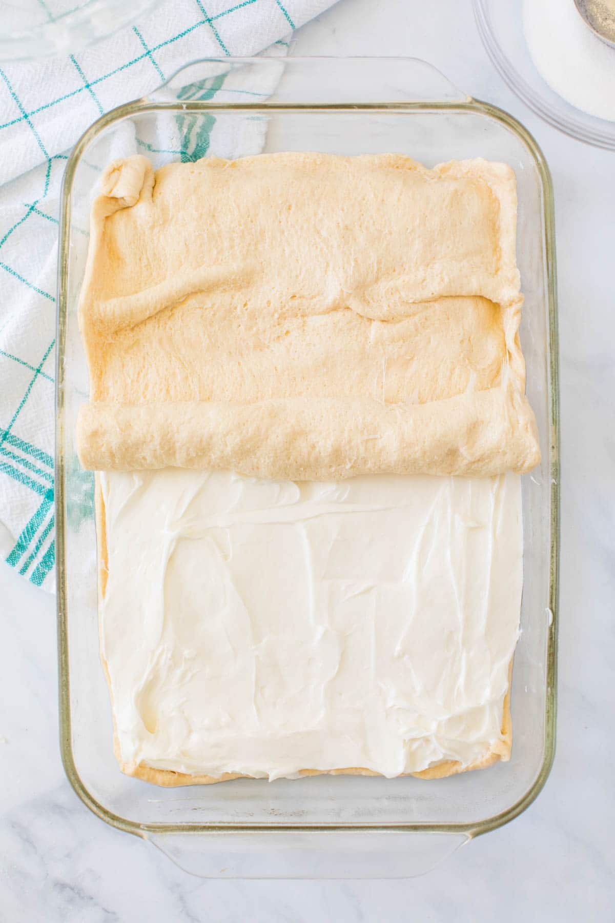 Crescent roll being laid on top of cream cheese in a baking dish