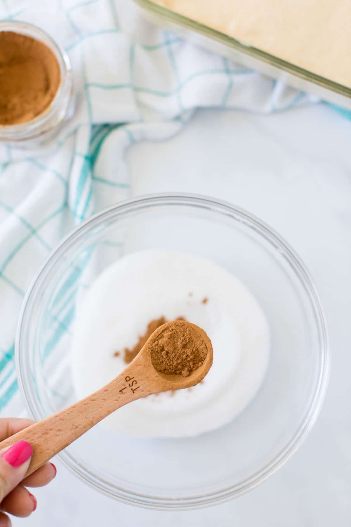 Spoon of cinnamon being held above a bowl of sugar