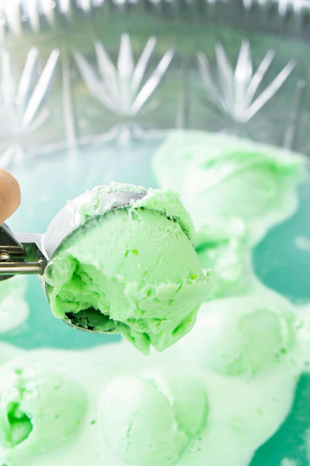 Hand adding a scoop of lime sherbet to a bowl of Halloween punch