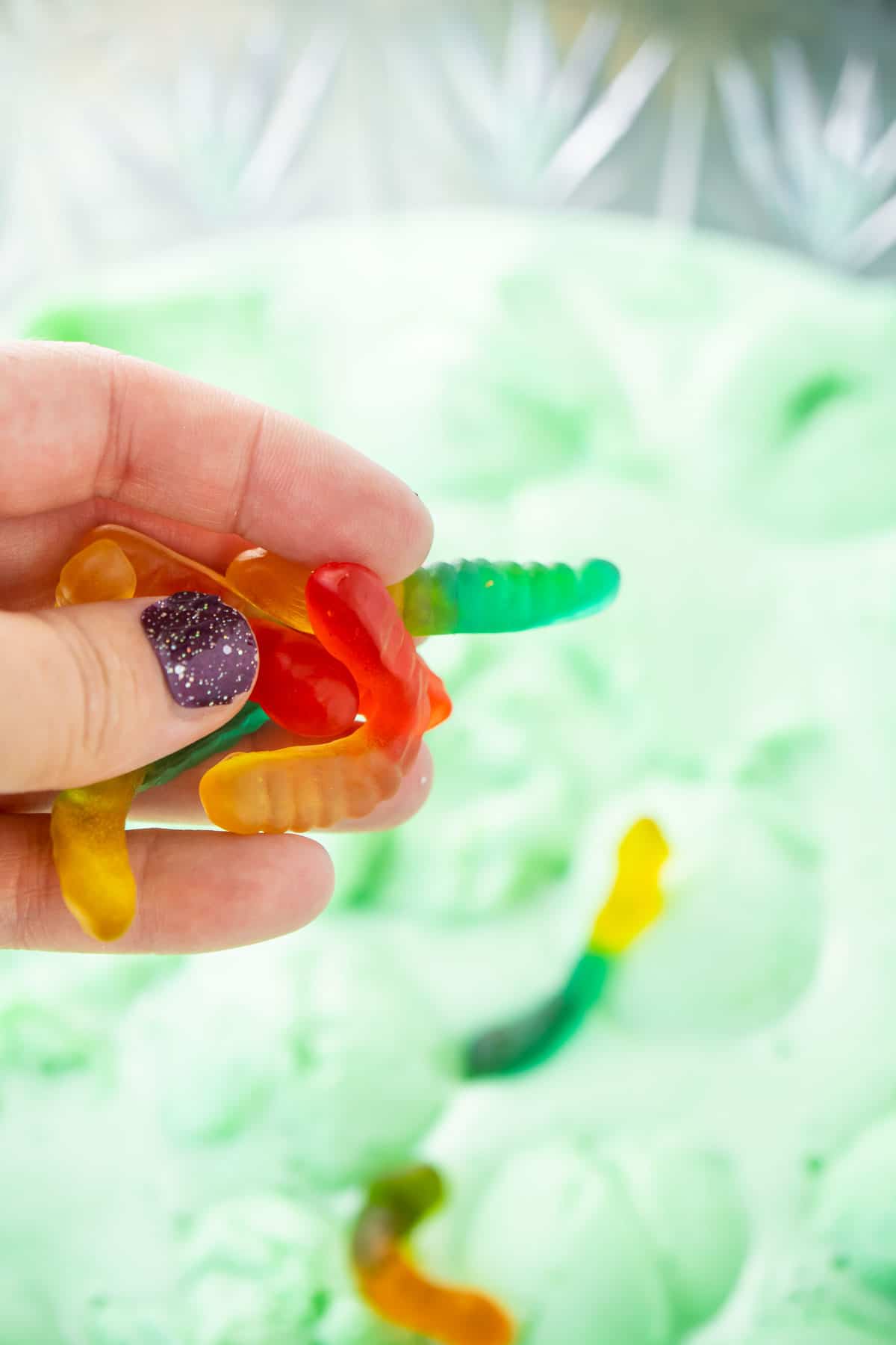 Hand adding gummy worms to a bowl of green Halloween punch