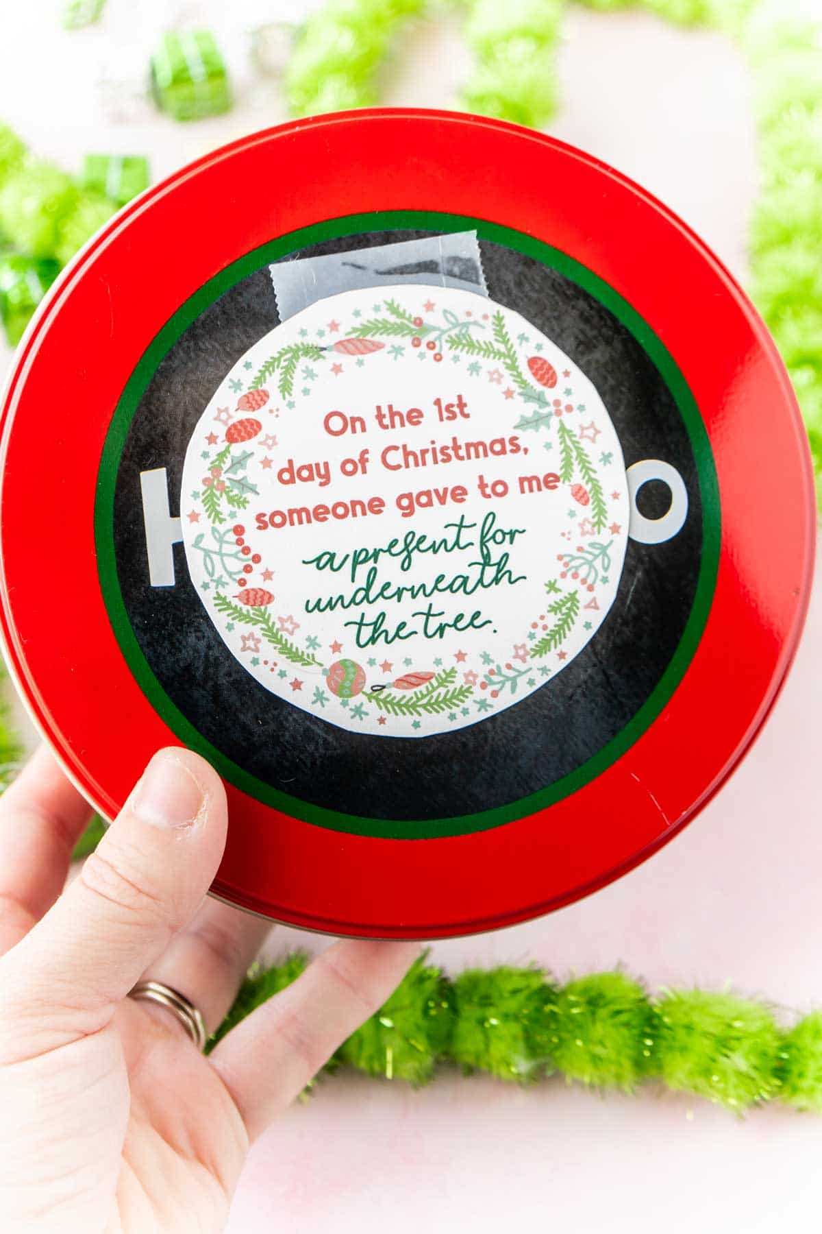 Woman's hand holding a tin with 12 days of christmas gifts inside