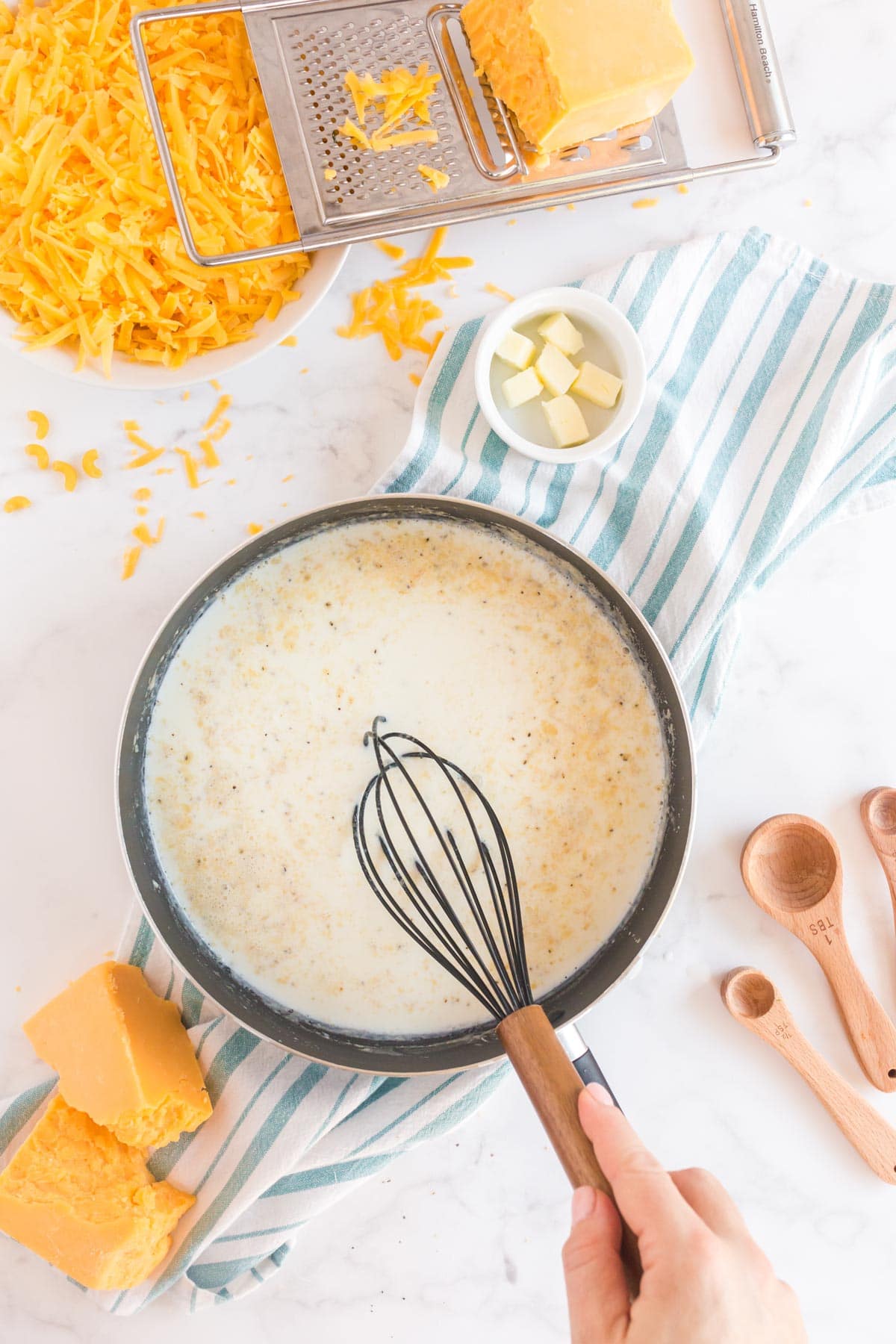 Woman's hand holding a whisk over a pan with milk and butter