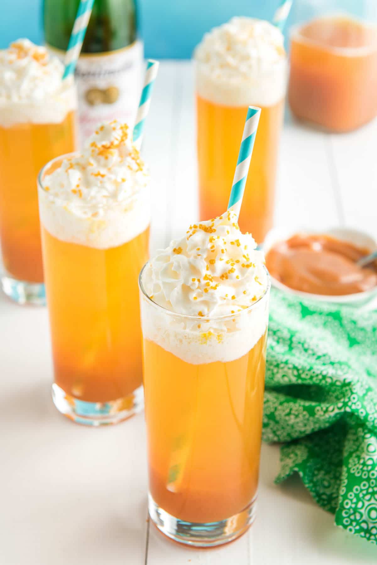 Four glasses with a caramel apple drink topped with whipped cream