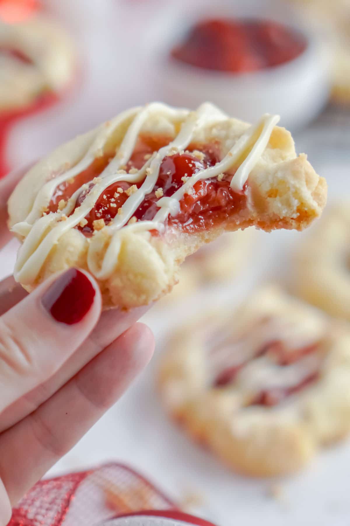 Hand holding a cherry cheesecake cookie with a bite taken out