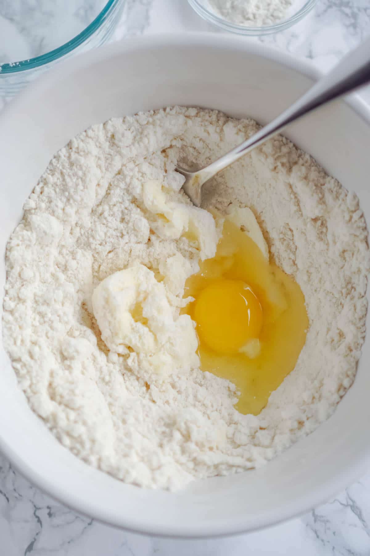 White bowl with sugar cookie mix and an egg in it