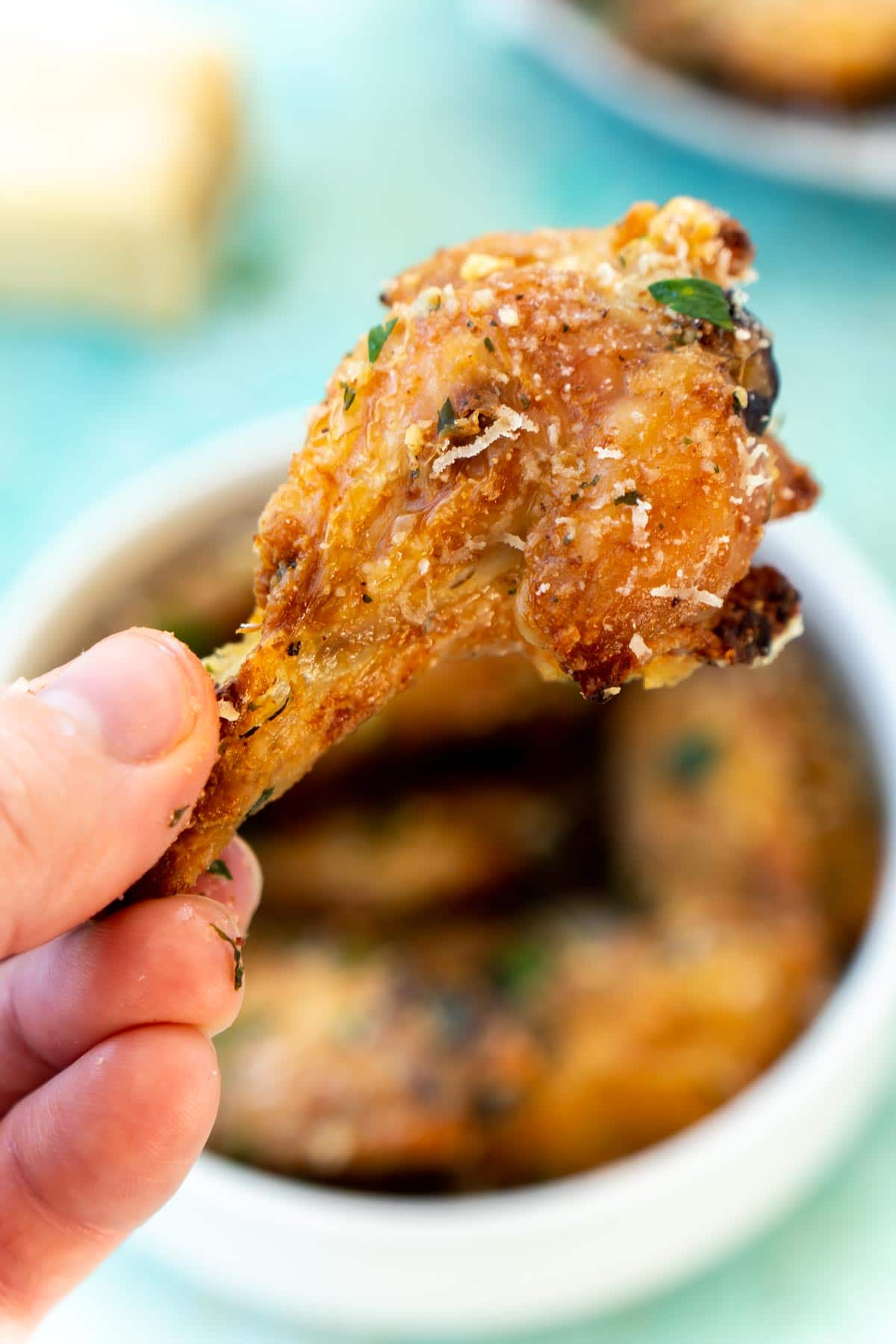 Hand holding one wing with a bowl of garlic parmesan wings in the background
