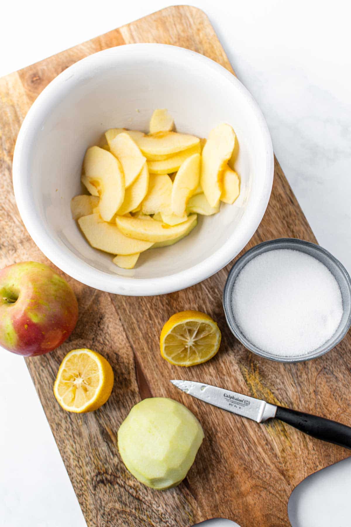 White bowl with sliced apples and lemon around the bowl