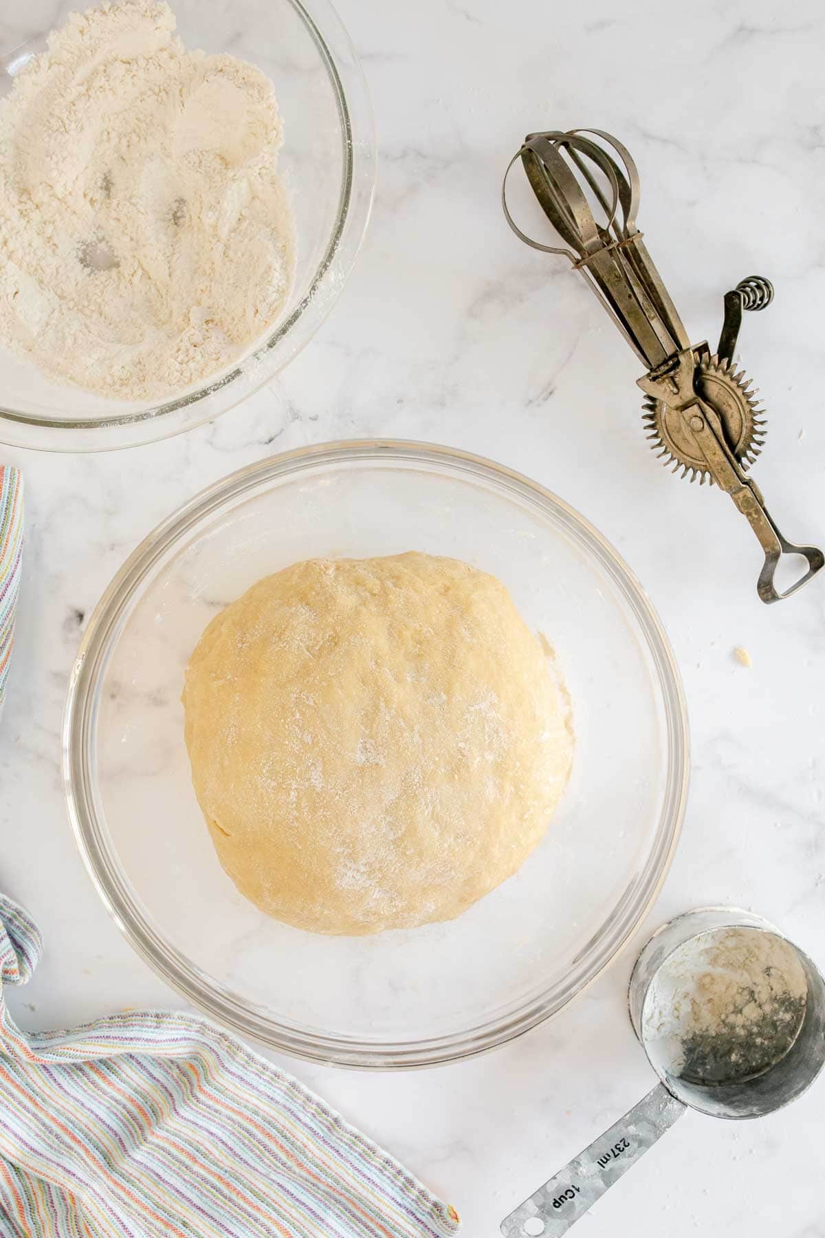 Dough for homemade crescent rolls in a glass bowl with a mixing cup on the side