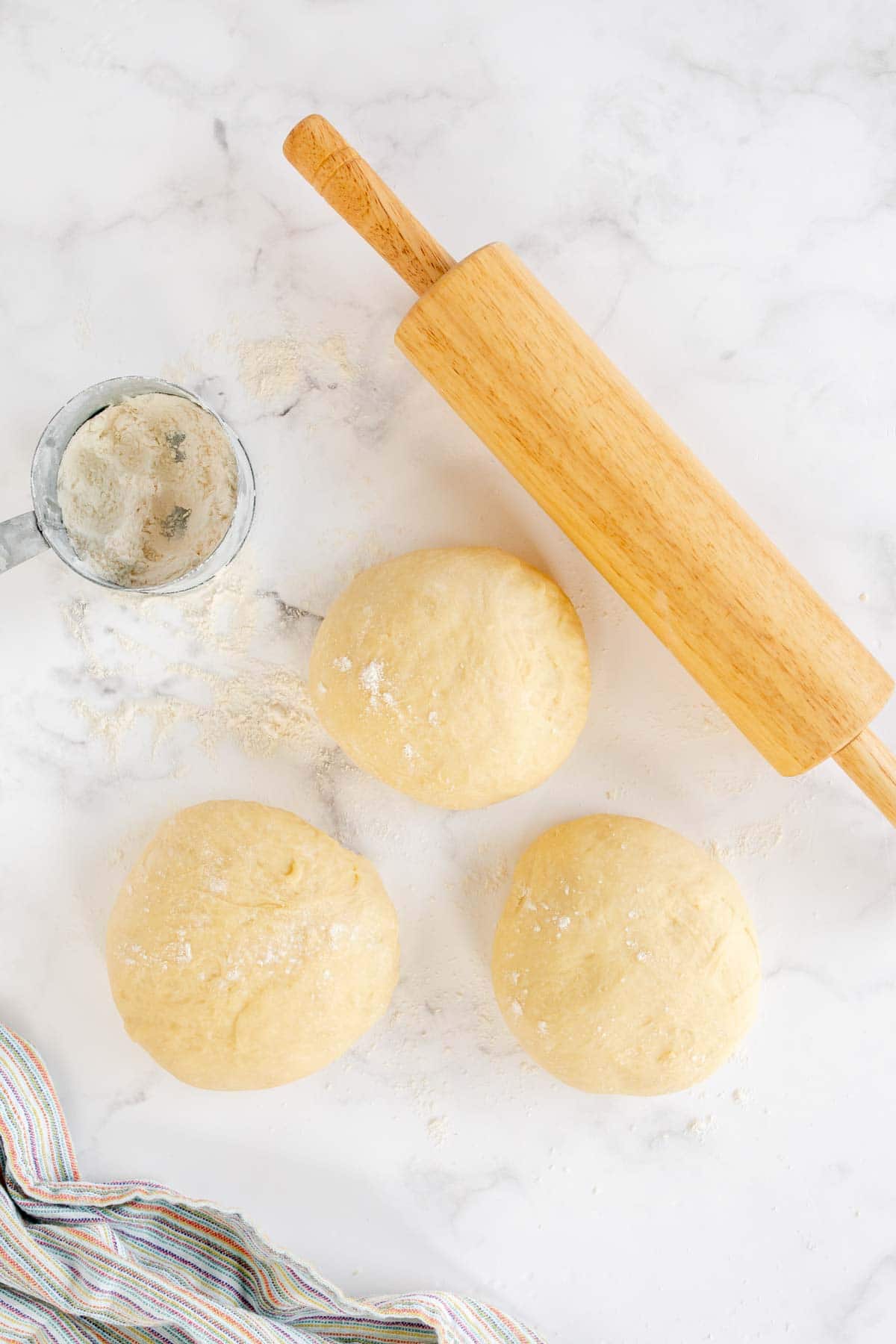 Three balls of homemade crescent roll dough with a rolling pin