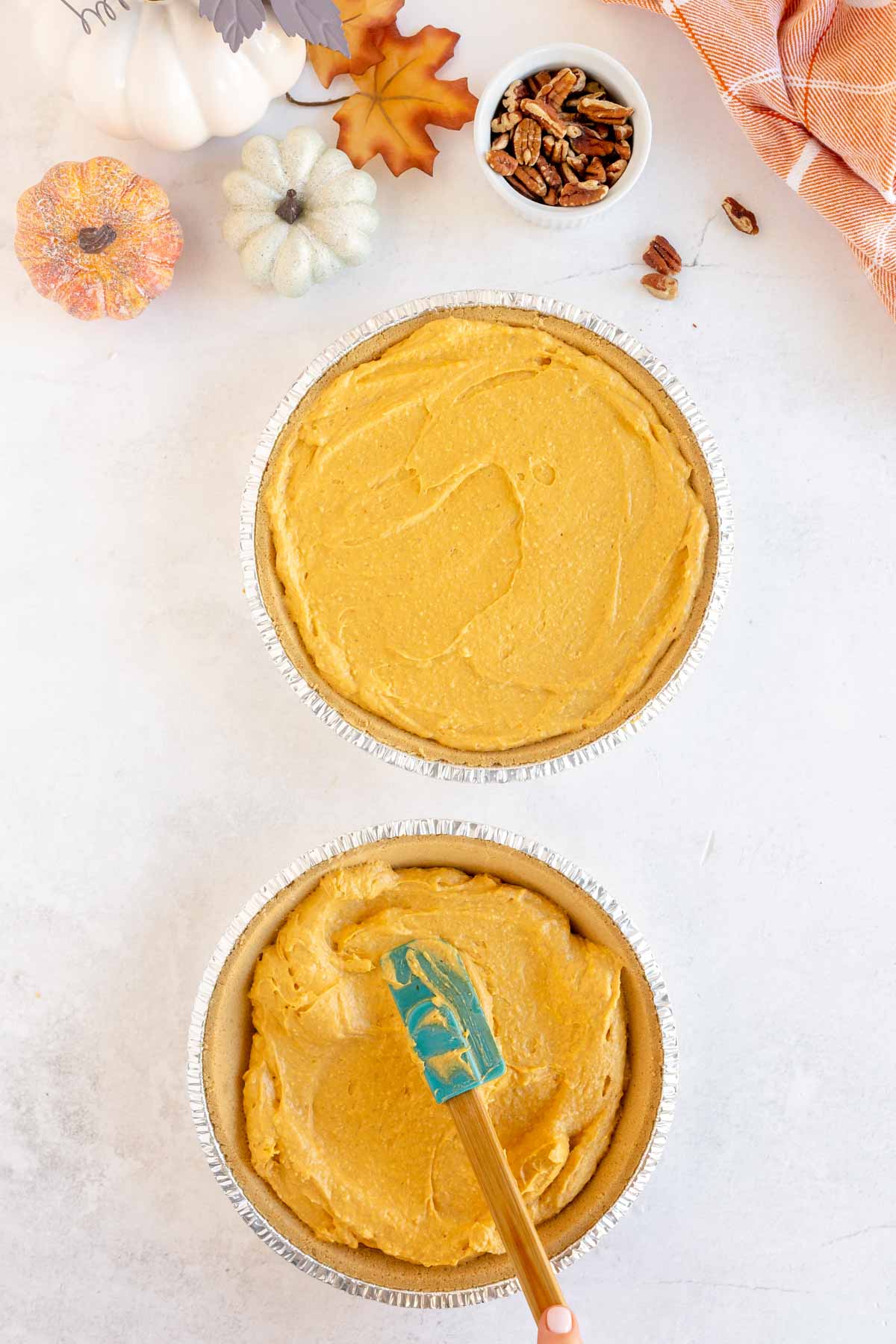 Spatula spreading pumpkin pie filling in graham cracker crusts