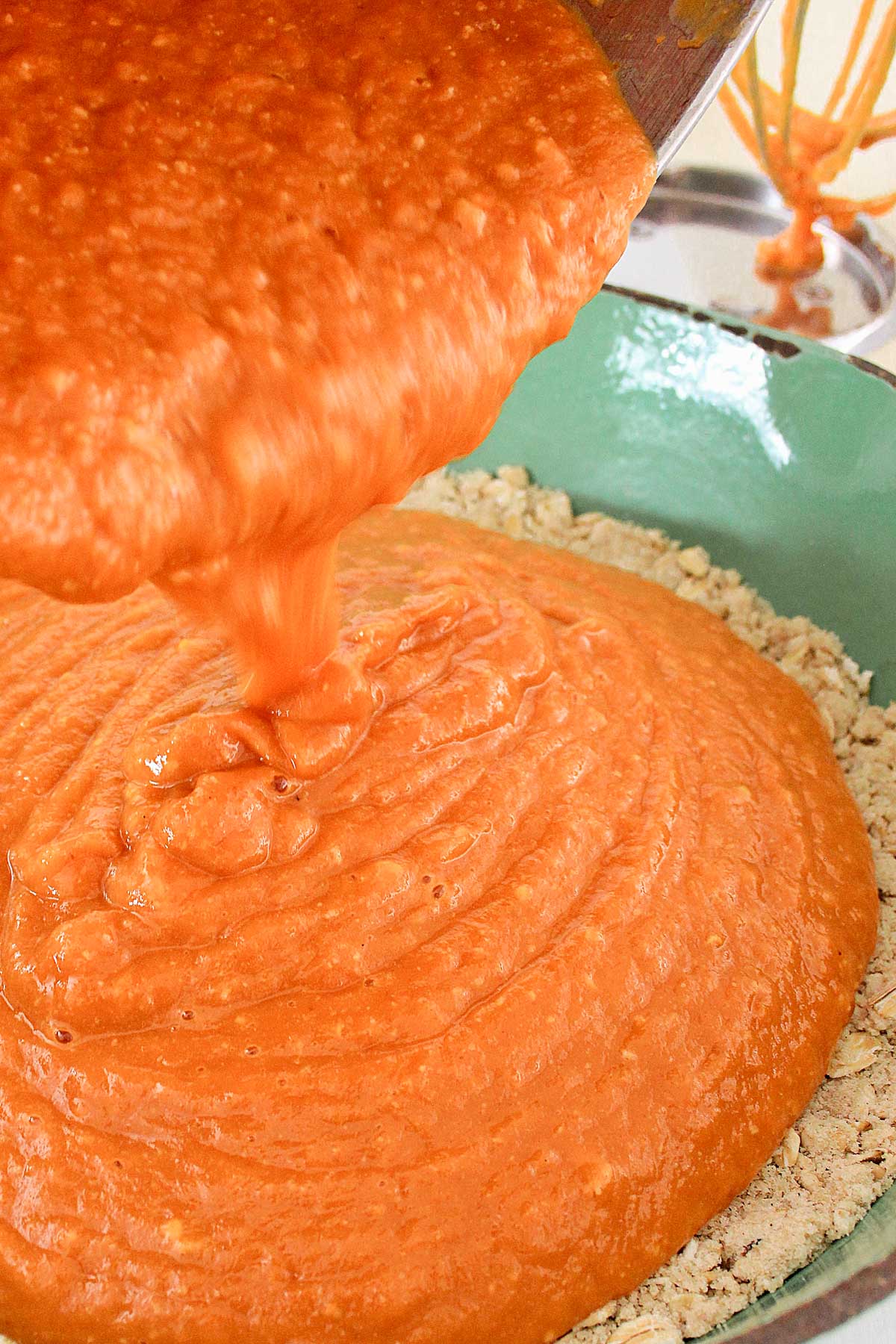 Bowl pouring pumpkin filling on top of pumpkin crisp topping