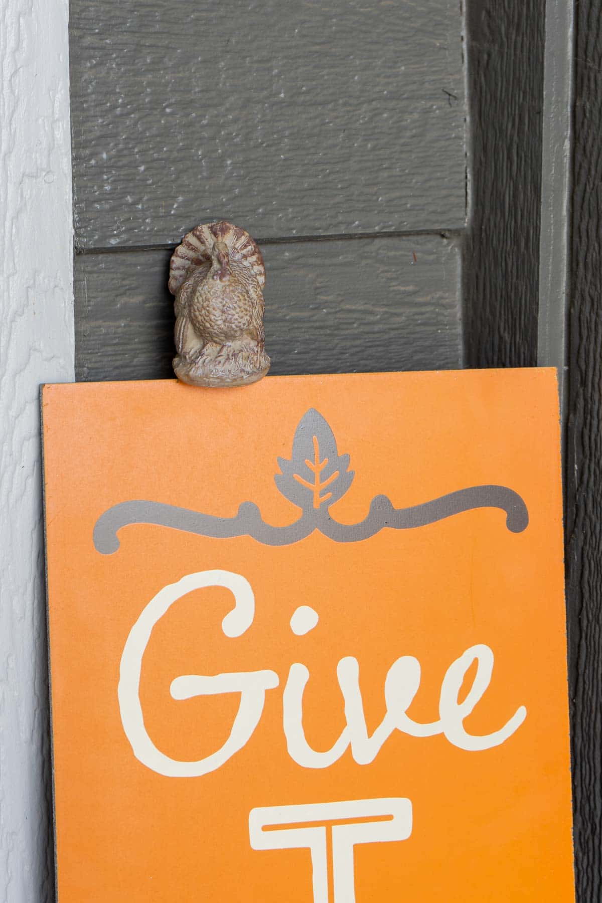 Ceramic turkey sitting on an orange give thanks sign