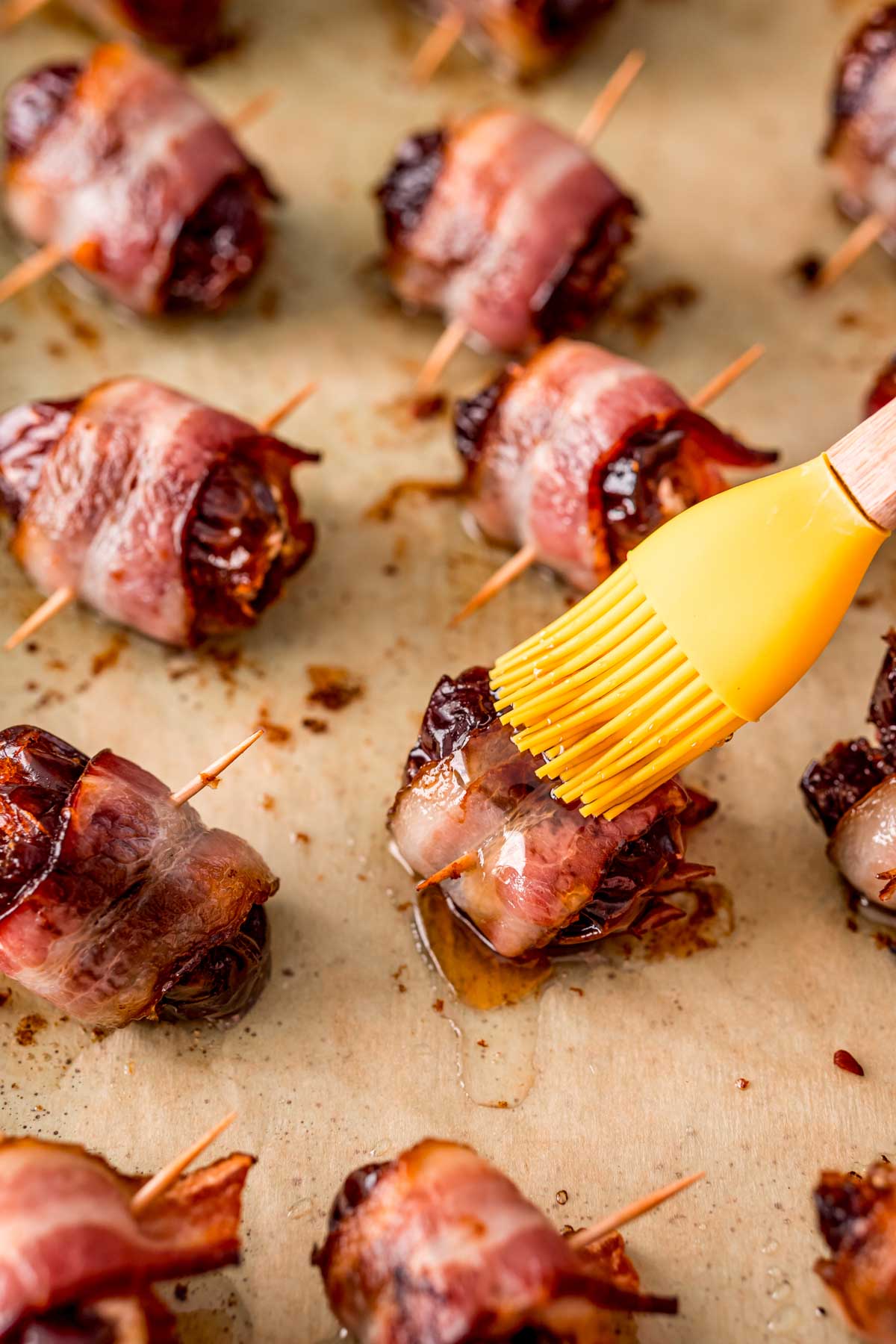 Bacon wrapped dates being brushed with maple syrup