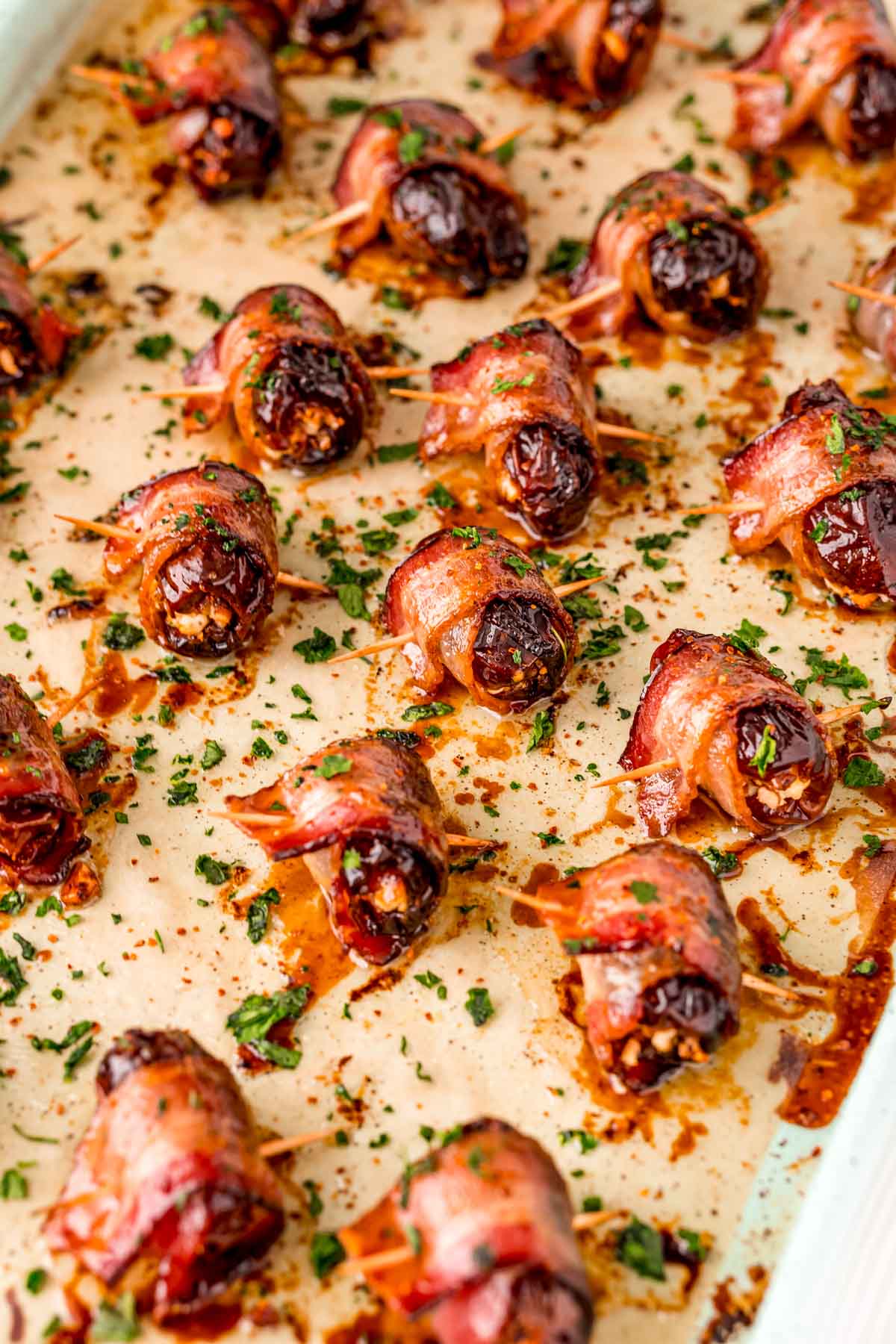 Baking sheet of bacon wrapped dates sprinkled with chili flakes and parsley