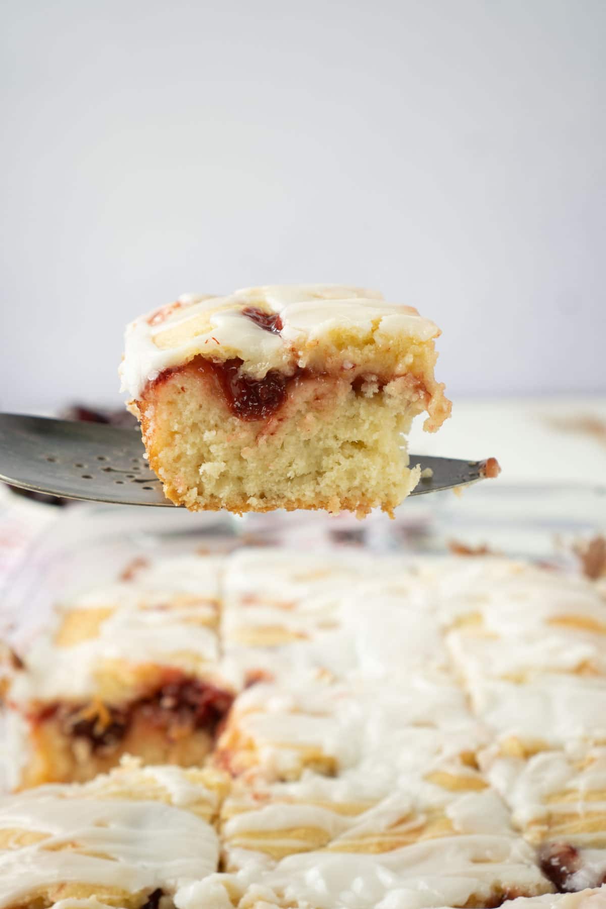 Spatula holding a piece of cherry cake above a pan of cherry cake