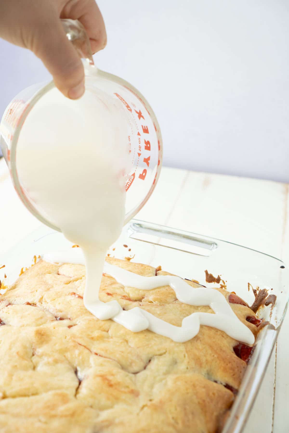 hand pouring icing on cherry cake top