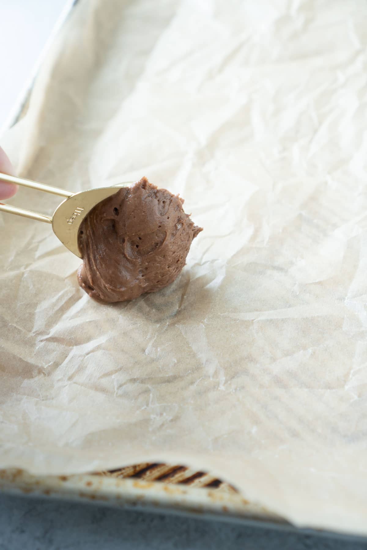 Gold teaspoon placing chocolate whoopie pie dough on a baking sheet