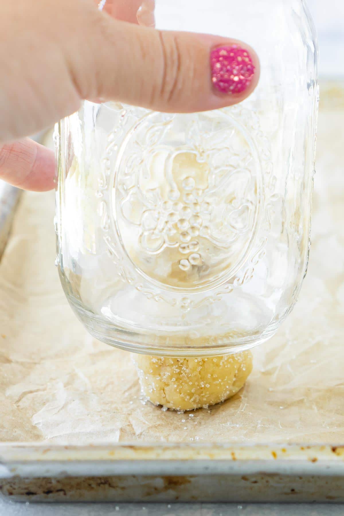 Mason jar pressing down on a ball of orange sugar cookie dough