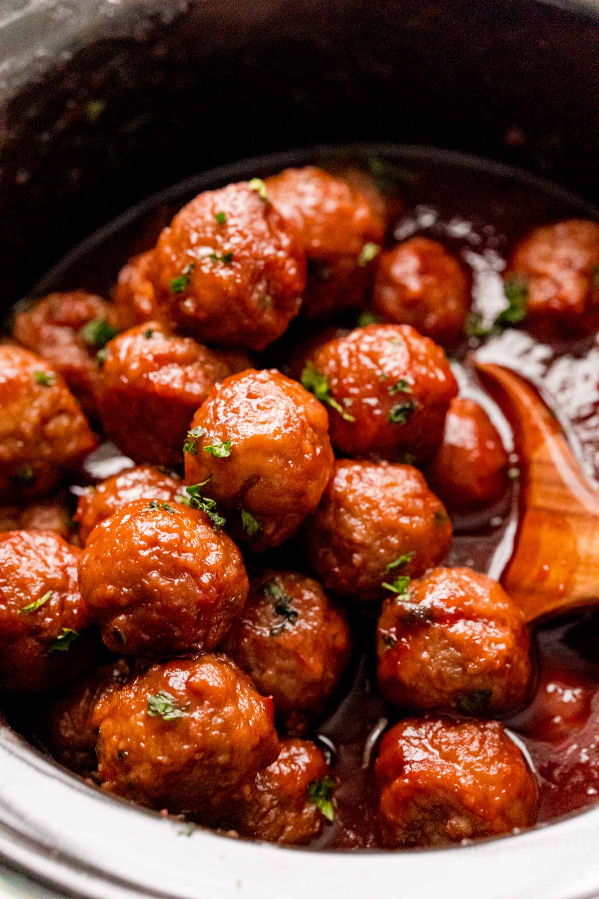 Crockpot grape jelly meatballs with a wooden spoon