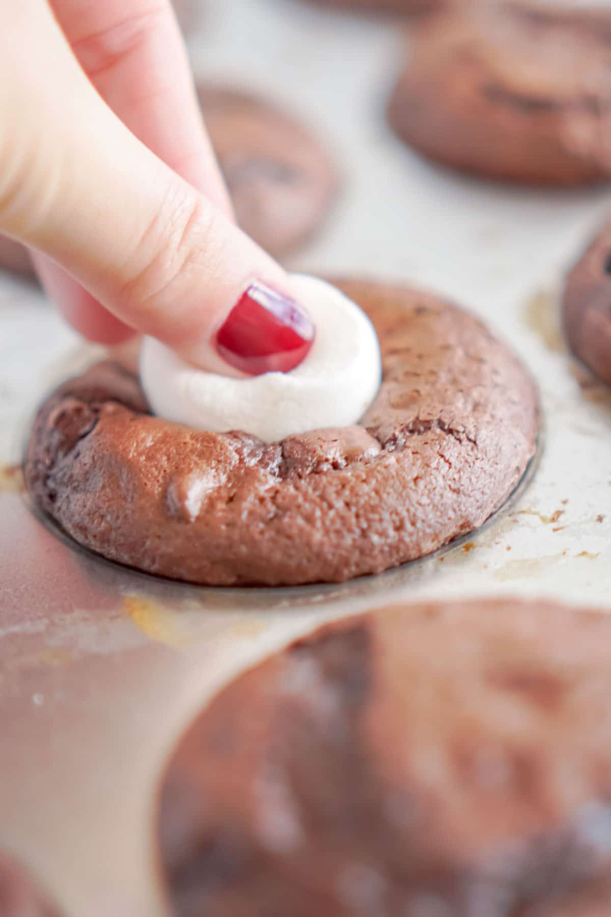 Woman's hand pressing a marshmallow on top of a chocolate cupcake