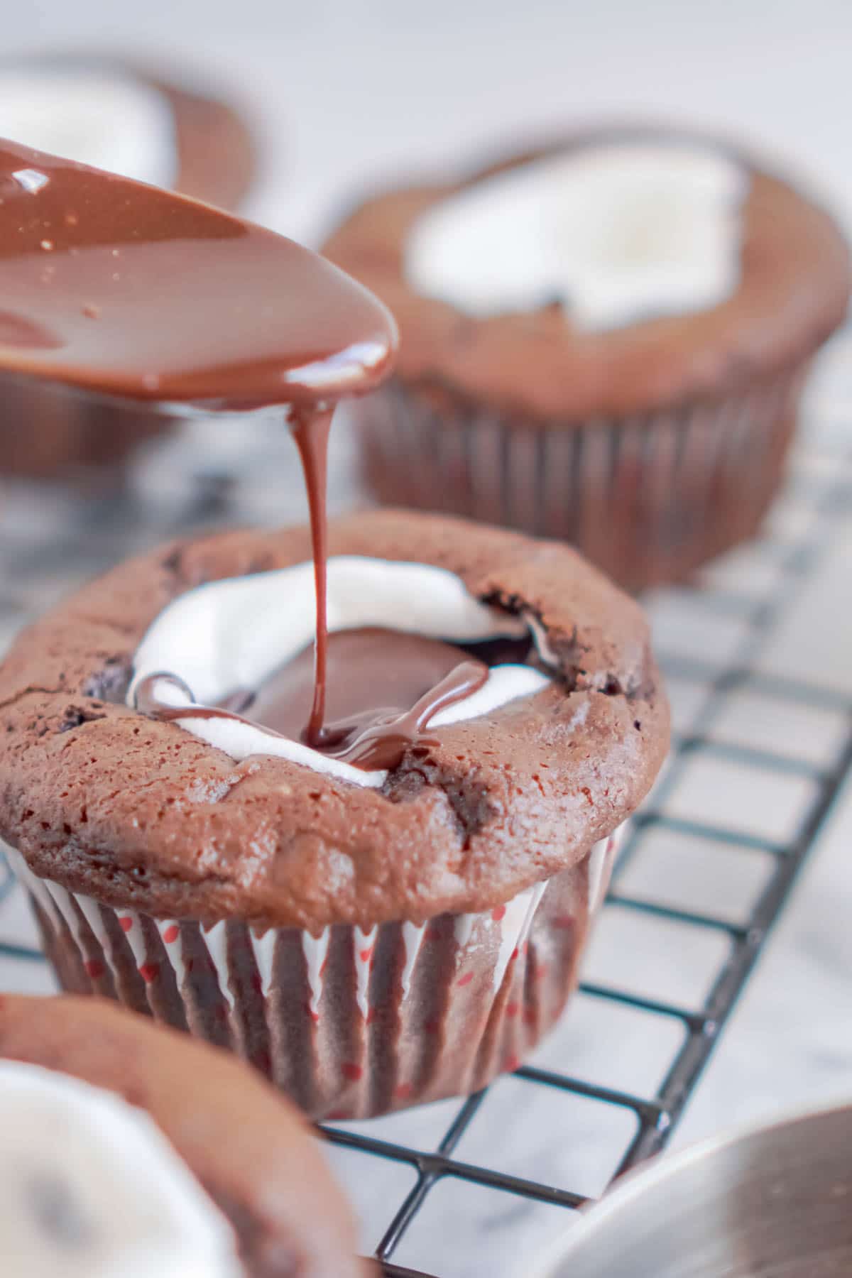 Spoon pouring chocolate glaze on chocolate cupcakes