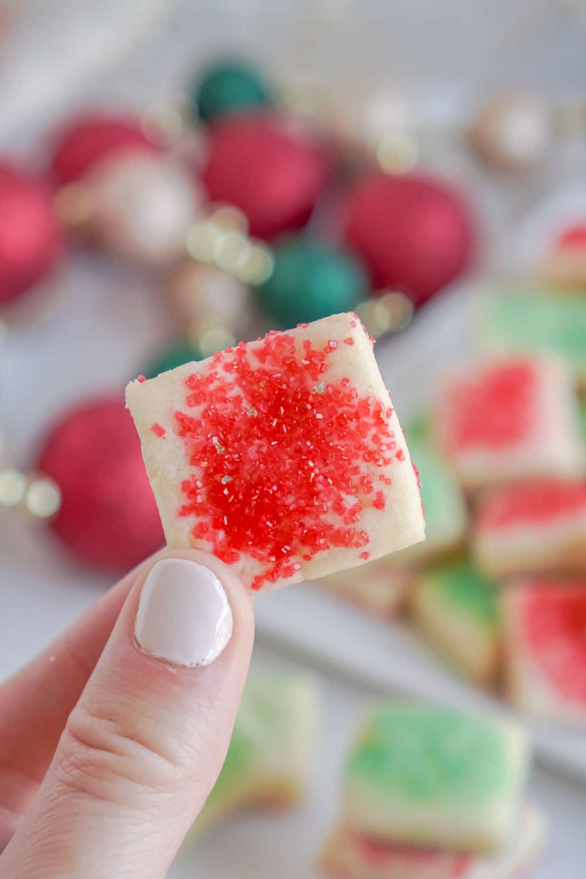 Hand holding a sugar cookie bite with ornaments in the background