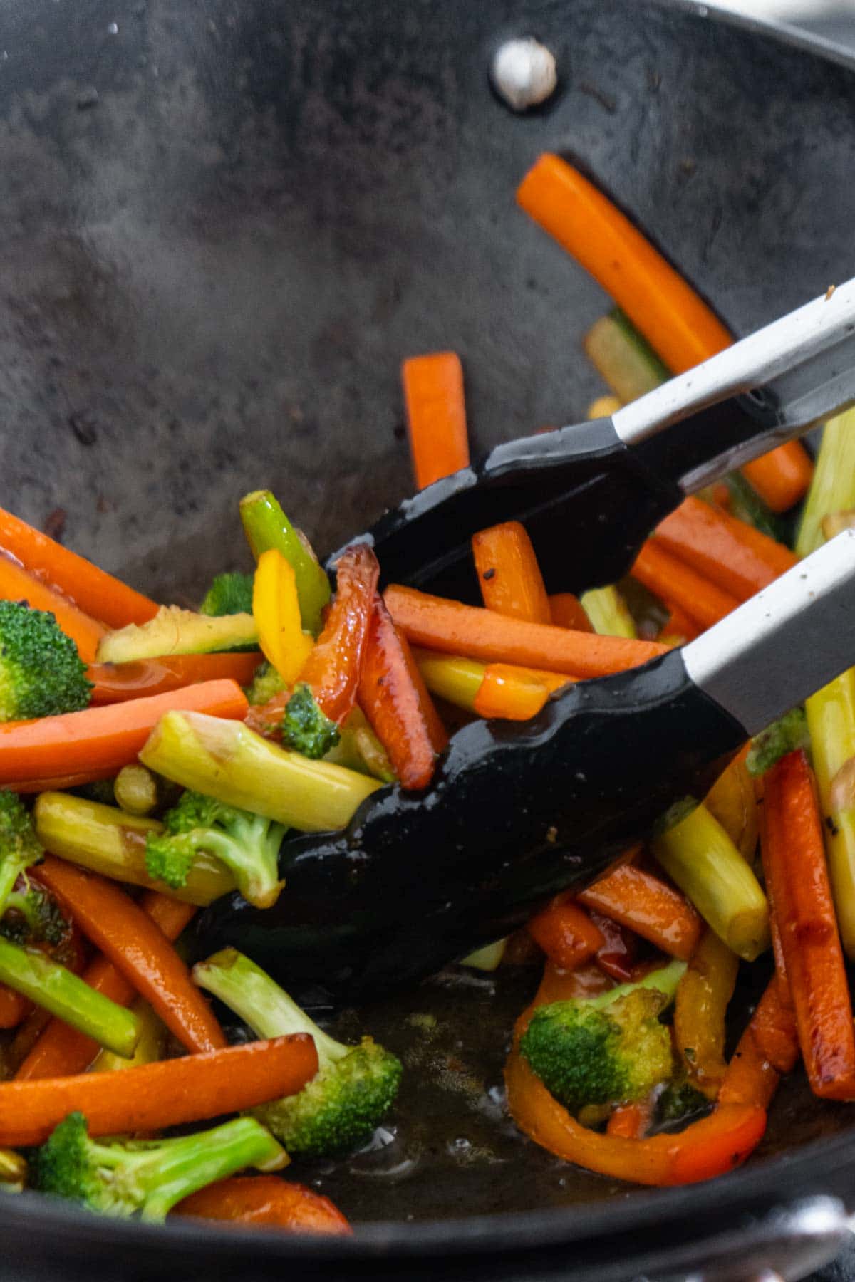 Sliced veggies in a wok with tongs