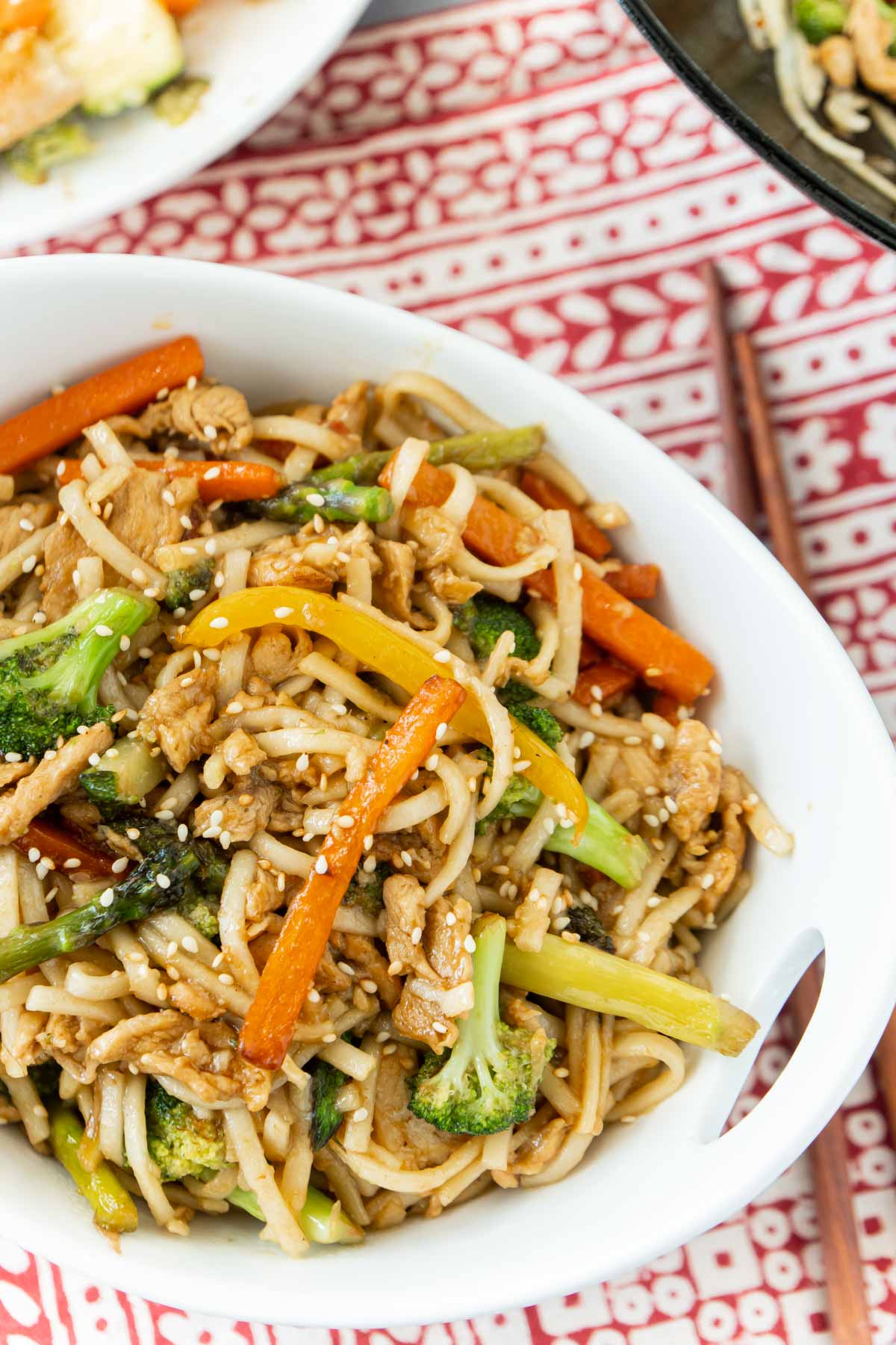 A white bowl with teriyaki chicken stir fry and chopsticks nearby