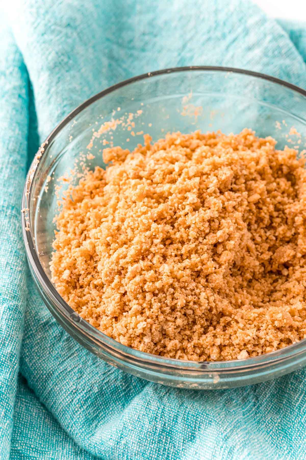 A glass bowl with graham cracker crust mixture in it