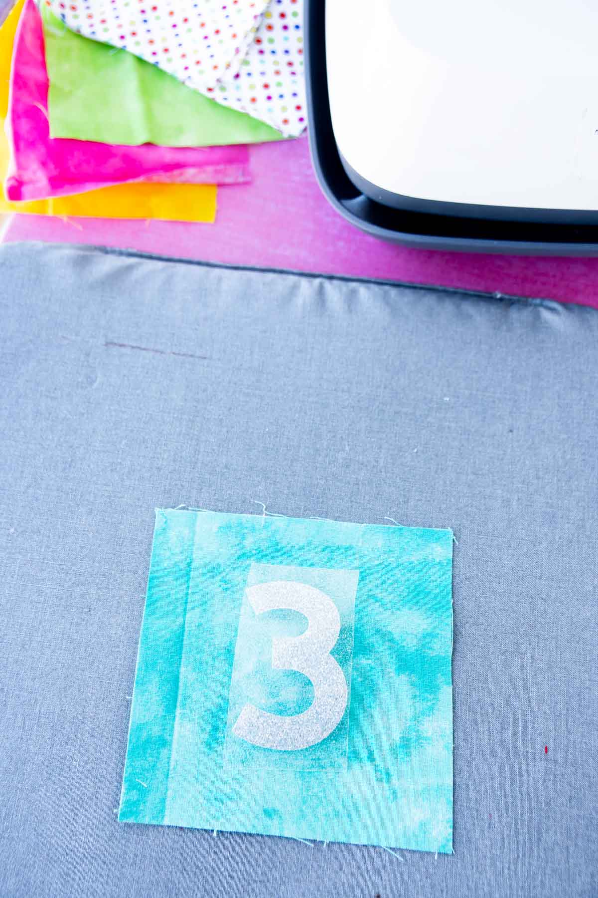 Fabric square with an iron on three on top of it