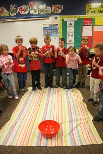 Kids standing around a beach towel with a bowl at the end