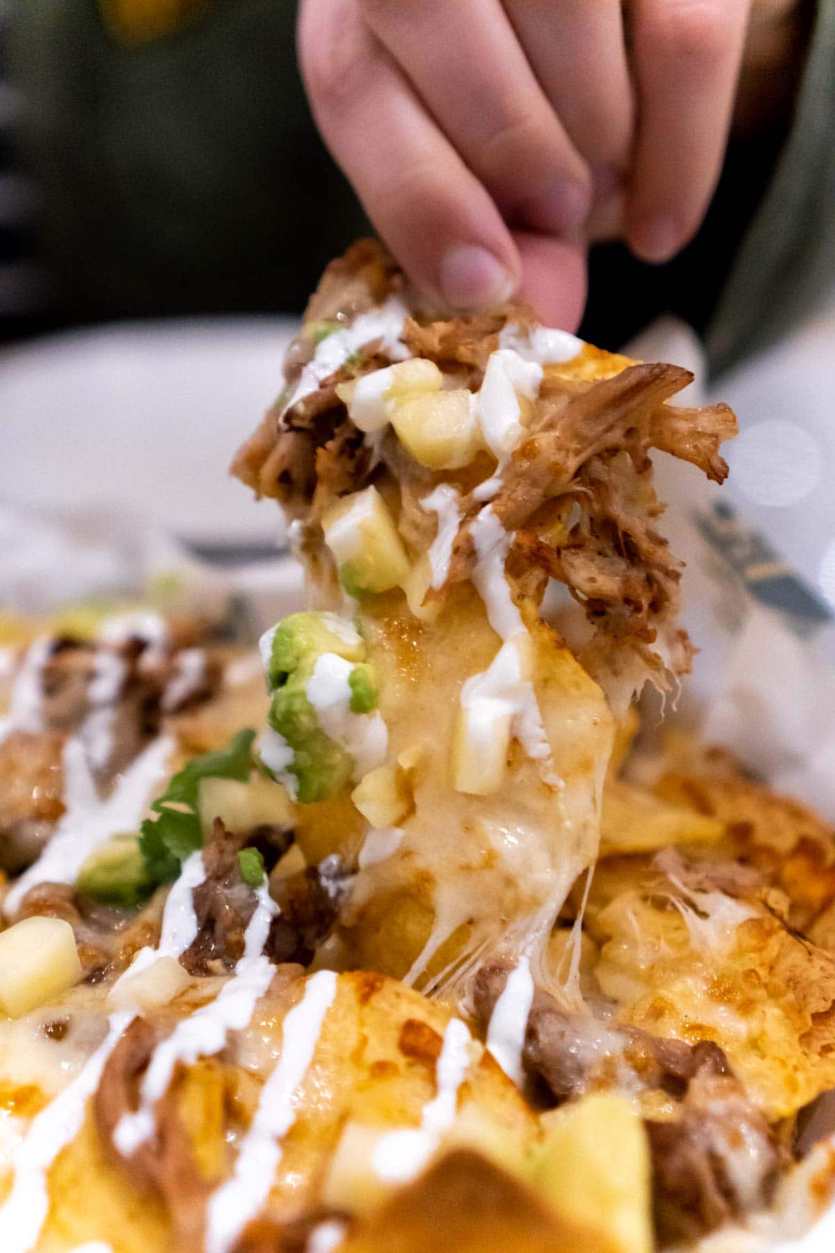 Woman's hand pulling a chip in carnitas nachos