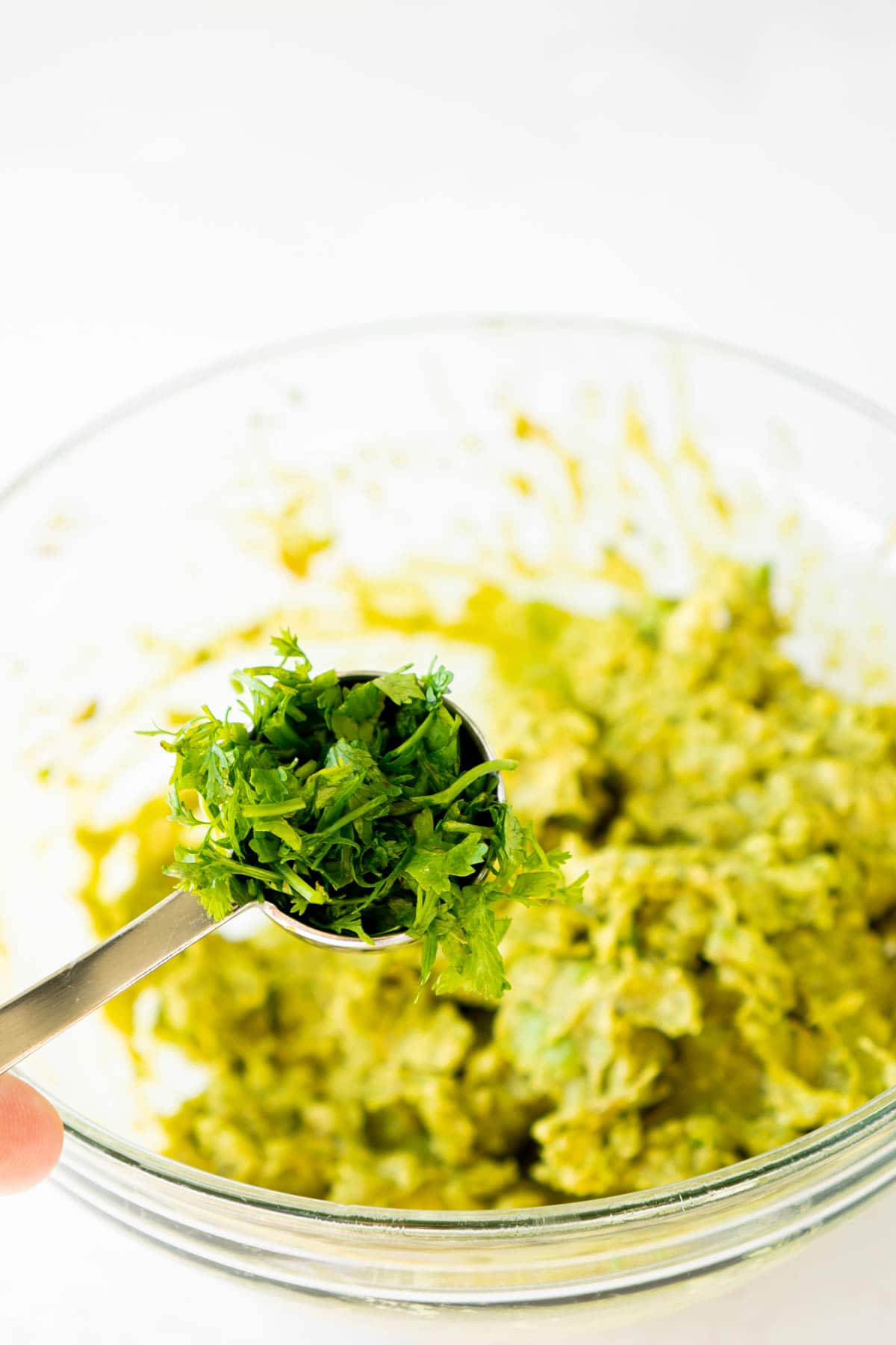 Tablespoon of cilantro above a bowl of guacamole